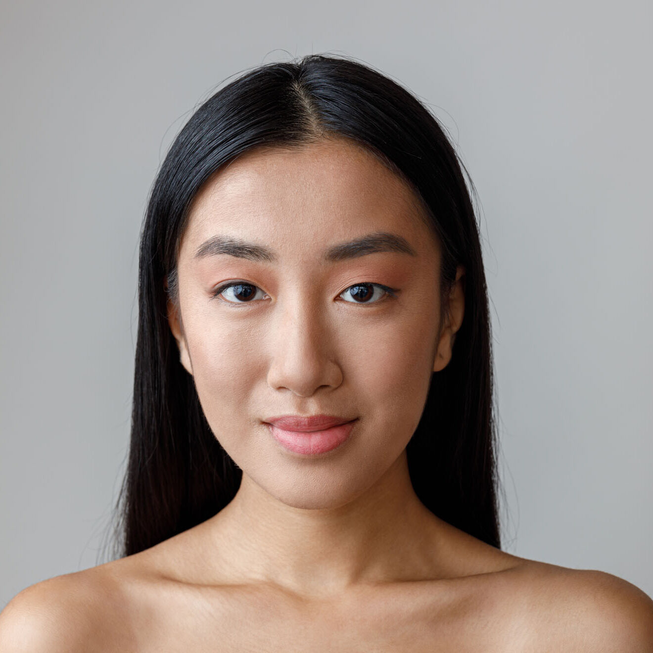 Close up of female person with perfect skin looking at camera and smiling. Isolated on light gray background